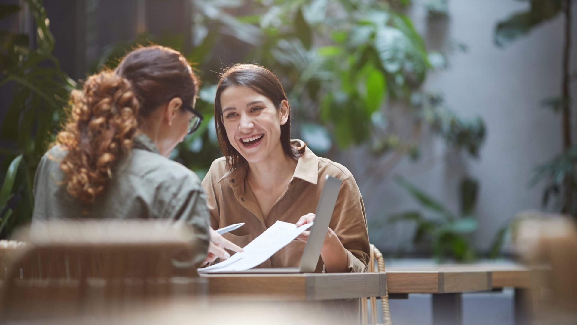 Portrait of cheerful young woman talking to friend or colleague during business meeting on outdoor cafe terrace, copy space